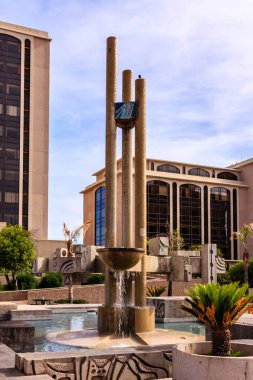 Üstünde saat olan uzun bir çeşme. Çeşme ağaçlar ve çalılarla çevrili.