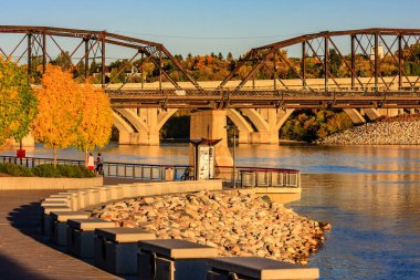 Bir köprü, arka planda bir şehir manzaralı bir nehri kapsar. Köprü taştan bir duvar ve bankla çevrili.