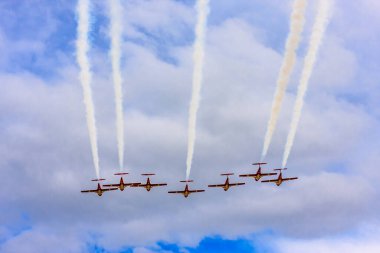 Bir grup uçak gökyüzünde düzenle uçuyor. Bulutlar beyaz ve gökyüzü mavi