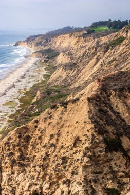 Okyanusa bakan kayalık bir uçurum. Kumsal kayalık ve su dalgalı. Uçurum bitki örtüsüyle kaplı ve sahil kumla kaplı.