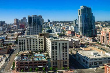 Oteli ve havuzu olan bir şehir manzarası. Otel çatısı havuzu olan büyük bir binadır. Şehir hareketli ve caddede bir sürü araba var.