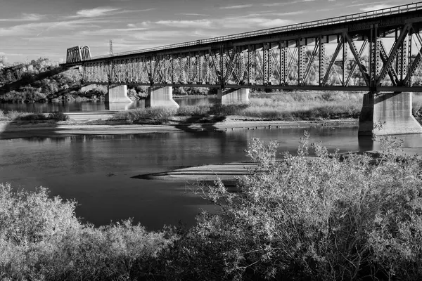 Köprü, arka planda bir köprü olan bir nehri kapsar. Köprü eski ve kırsal bir görünüme sahip. Su sakin ve köprü ağaçlarla çevrili.