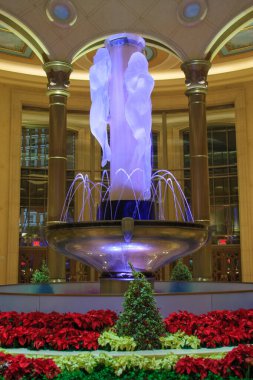 Ortasında beyaz bir melek heykeli olan büyük bir çeşme. Çeşme kırmızı ve sarı çiçeklerle çevrilidir.