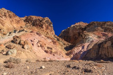 Arka planda mavi gökyüzü olan kayalık bir dağ sırası. Dağlar kahverengi ve gri renklerin karışımıdır.