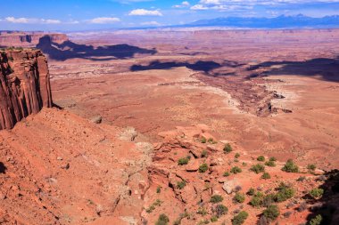 Arkasında dağ olan bir çöl manzarası. Gökyüzü açık ve güneş parlıyor.