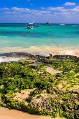 Kayalık bir kıyıya yakın suda bir tekne var. Su mavi ve gökyüzü berrak.