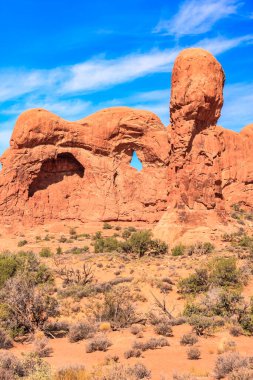 Büyük bir kaya oluşumu ve ortasında küçük bir delik olan bir çöl manzarası. Gökyüzü açık ve mavi