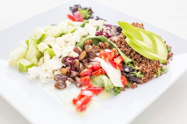 Salata, kinoa ve elmalı bir tabak yemek. Salata fındık ve domatesle kaplı.