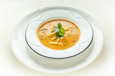 Bir kase yeşil otlu çorba, üstüne de garnitür. Çorba beyaz tabakta servis edilir.