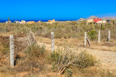 Çitleri ve birkaç ağacı olan çorak bir çöl manzarası. Gökyüzü mavi ve güneş parlıyor.