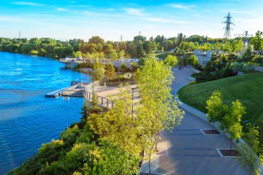 İçinden nehir akan bir park. Park ağaçlarla dolu ve nehir boyunca uzanan bir patikası var.