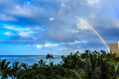 Bir plajın üzerindeki gökkuşağında bir gökkuşağı görülür. Gökyüzü bulutlu ve arkada okyanus var.