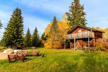 Kırsal bir kulübe yemyeşil bir tarlada, yanında bir bank ve birkaç sandalye ile duruyor. Kulübe ağaçlarla çevrili ve gökyüzü açık ve mavi. Barış ve sükunet kavramı