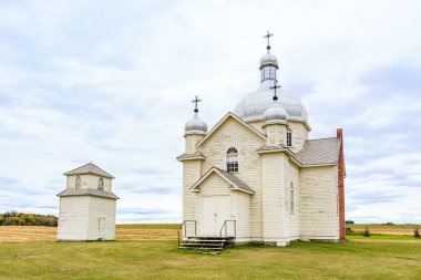 Uzun çan kulesi olan küçük beyaz bir kilise bir tarlada oturur. Kilise birkaç küçük binayla çevrilidir. Gökyüzü bulutlu ve çimenler yeşil