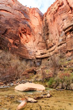 İçinden nehir akan kayalık bir kanyon. Kanyon ağaçlar ve kayalarla dolu ve su berrak ve sakin. Huzurlu ve huzurlu bir sahne.