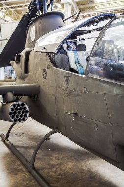 Bir hangarda askeri helikopter sergileniyor. Kokpit açık ve pilot kokpitte oturuyor.