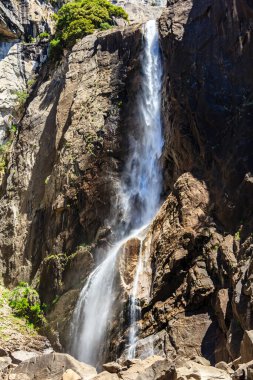 Bir şelale kayalık bir uçurumdan aşağı akıyor. Su berrak ve kayalar kahverengi. Huzurlu ve huzurlu bir sahne.