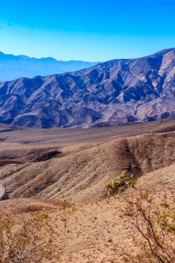 Arka planda açık mavi gökyüzü olan bir dağ sırası. Dağlar kahverengi toprakla kaplı ve gökyüzü parlak mavi
