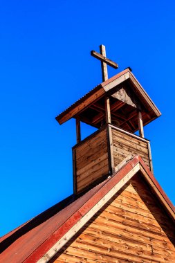 Üstünde haç olan bir kilise kulesi. Haç ahşaptan yapılmıştır ve çan kulesinin üzerine yerleştirilir. Gökyüzü mavi ve berrak, ve güneş parlıyor.