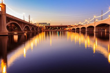 Bir köprü alacakaranlıkta bir nehri kapsar. Su sakin ve gökyüzü güzel bir mavi.