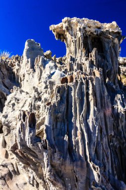 Arka planda mavi gökyüzü olan kayalık bir uçurum. Uçurum büyük kayalardan yapılmıştır ve pürüzlü bir dokusu vardır.