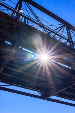Parlayan güneşli bir köprü. Güneş parlıyor ve gökyüzü açık. Köprü eski ve bir sürü metal var.