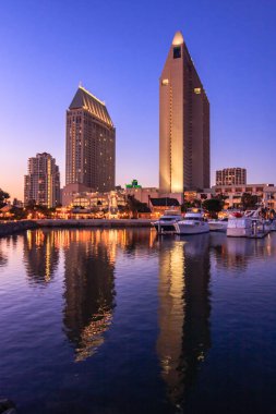 Büyük bir oteli ve arka planda büyük bir binası olan bir şehir silueti. Su sakin ve gökyüzü güzel bir mavi.