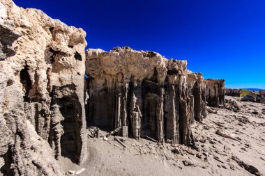 Arka planda mavi gökyüzü olan kayalık bir uçurum. Uçurum kumtaşından yapılmıştır ve üzerinde bir sürü delik vardır.