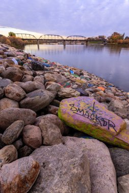 A rock with the word smacker written on it is sitting on a pile of rocks by a body of water clipart