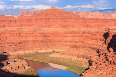 Arka planda dağlar olan bir nehir bir kanyonun içinden akar. Kanyon kayalarla dolu ve nehir sakin.