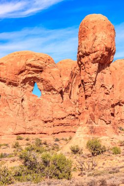 Ortasında küçük bir delik olan büyük bir kaya oluşumu. Gökyüzü mavi ve güneş parlıyor.