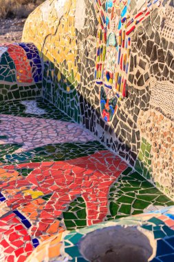 Üzerinde el olan bir mozaik bank. Yedek kulübesi renkli ve eşsiz bir tasarımı var. Banktaki el kırmızı ve yeşil, ve uzanıyor gibi görünüyor. Bankta bir çöl var.