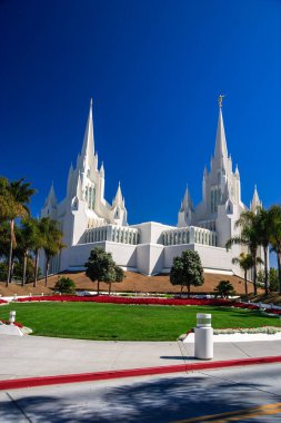 Beyaz kilisenin iki uzun kulesi vardır ve ağaçlarla çevrilidir. Gökyüzü mavi ve berrak