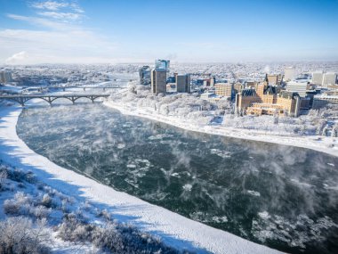 Saskatoon şehir merkezinin kışın yüksek çözünürlüklü hava aracı görüntüsü, karla kaplı bir şehir manzarası, donmuş Güney Saskatchewan Nehri ve soğuk çatılar. Mevsimin dingin güzelliğini yakalamak için bu görüntü turizm promosyonları için idealdir.