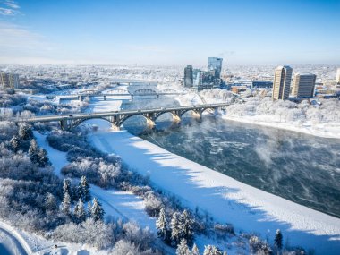 Saskatoon şehir merkezinin kışın yüksek çözünürlüklü hava aracı görüntüsü, karla kaplı bir şehir manzarası, donmuş Güney Saskatchewan Nehri ve soğuk çatılar. Mevsimin dingin güzelliğini yakalamak için bu görüntü turizm promosyonları için idealdir.