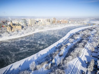 Saskatoon şehir merkezinin kışın yüksek çözünürlüklü hava aracı görüntüsü, karla kaplı bir şehir manzarası, donmuş Güney Saskatchewan Nehri ve soğuk çatılar. Mevsimin dingin güzelliğini yakalamak için bu görüntü turizm promosyonları için idealdir.