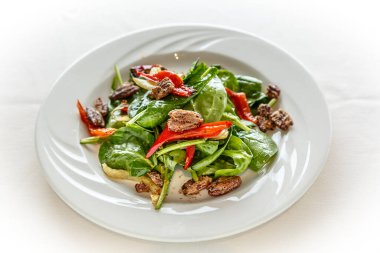 Ispanaklı salata, kırmızı biber ve beyaz tabakta fındık. Salata beyaz bir masa örtüsünde servis edilir.