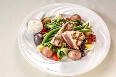 Beyaz tabağı ve beyaz kasesi olan bir tabak yemek. Tabakta beyaz soslu salata ve bir parça et var.