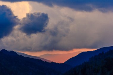 Gökyüzü bulutlu ve güneş batıyor. Dağlar arka planda ve gökyüzü mavi ve turuncu karışımı.