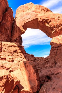 Arka planda mavi gökyüzü olan büyük bir kaya kemeri. Kemer yolu kızıl kayadan yapılmıştır ve gökyüzüne açıktır.