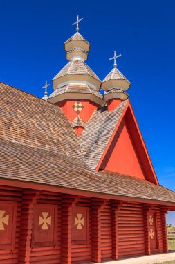 Arka planda mavi gökyüzü olan kırmızı bir kilise. Kilisenin üstünde bir haç var.