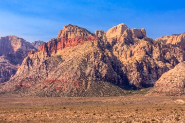 Dağlar kırmızı ve kahverengidir ve gökyüzü mavidir. Dağlar çok yüksek ve gökyüzü çok berrak.
