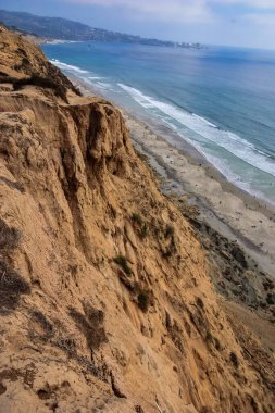 Kayalık bir uçurum büyük bir su kütlesiyle sahile bakar. Sahil, manzaranın ve okyanusun tadını çıkaran insanlarla dolu.