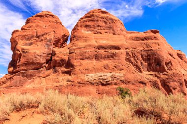 Arka planda mavi gökyüzü olan kayalık bir dağ. Dağ kırmızı kayalardan yapılmıştır ve çok fazla dokusu vardır.