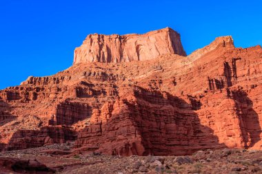 Kırmızı kaya yüzlü ve arkasında mavi gökyüzü olan bir dağ. Dağ çok yüksek ve gökyüzü açık ve mavi.