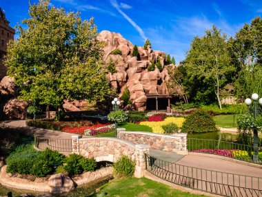 Köprüsü ve kaya duvarı olan bir park. Köprü taştan yapılmıştır ve kaya duvarı taştan yapılmıştır. Park çiçekler ve ağaçlarla dolu.