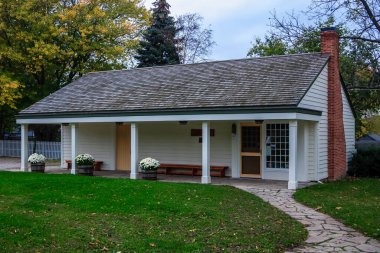 Verandası ve bacası olan küçük beyaz bir ev. Ev yemyeşil bir çimenlikle çevrili.