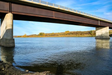 Bir köprü nehri sakin ve berrak bir suyla kaplar. Köprü beton ve çelikten yapılmıştır.