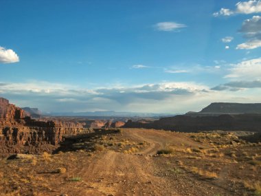 Ortasında toprak yol olan bir çöl manzarası. Gökyüzü birkaç bulutla mavidir