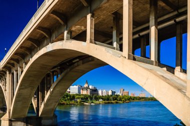 Bir köprü, arka planda bir şehir olan bir nehri kapsar. Köprü, sudan görülebilen büyük, kemerli bir yapıdır.